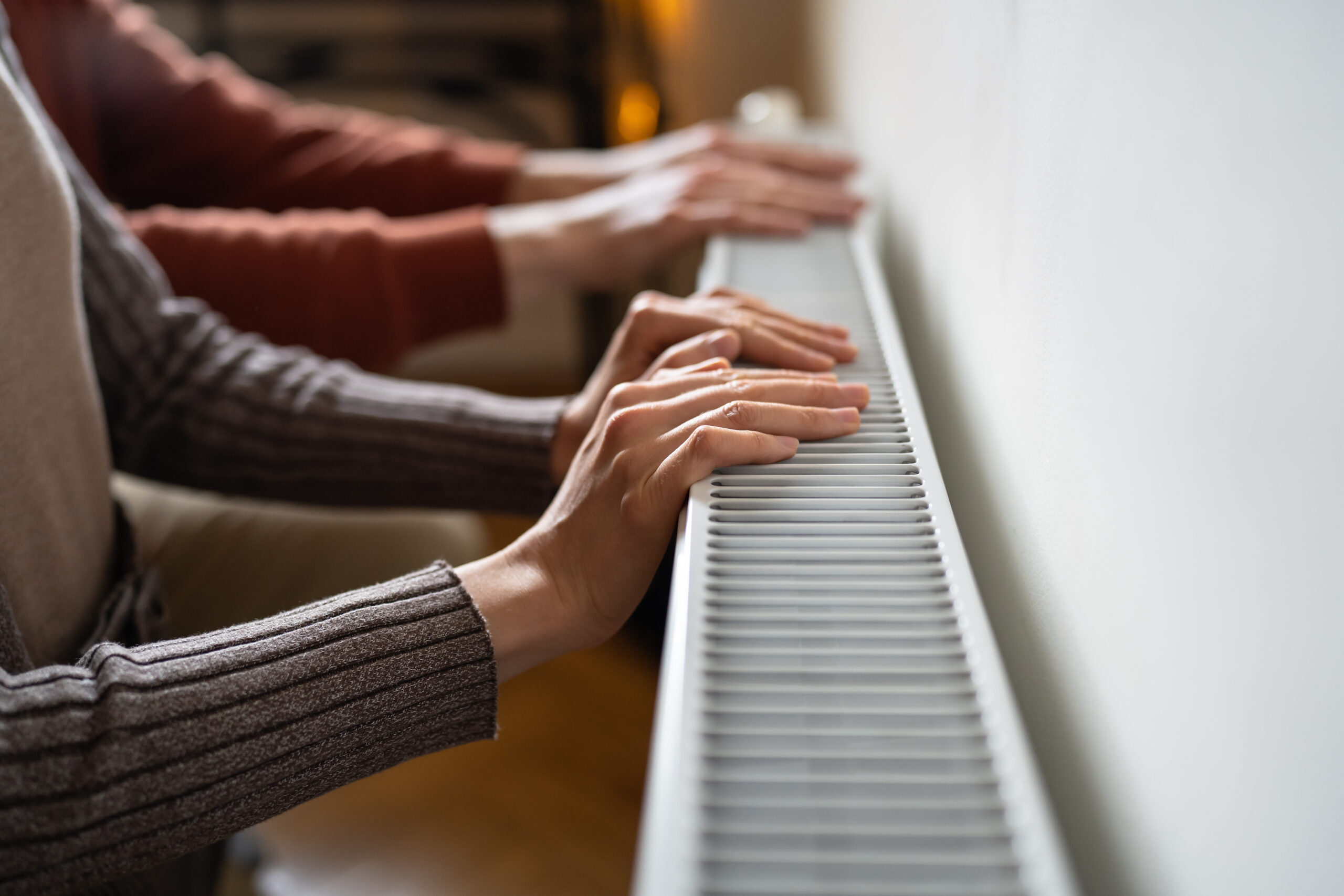 Hands suffering from lack of heat checking temperature electric battery. Palms warming at home radiator. Expensive energy resources, energy crisis in Europe. Saving gas, High price in heating season.