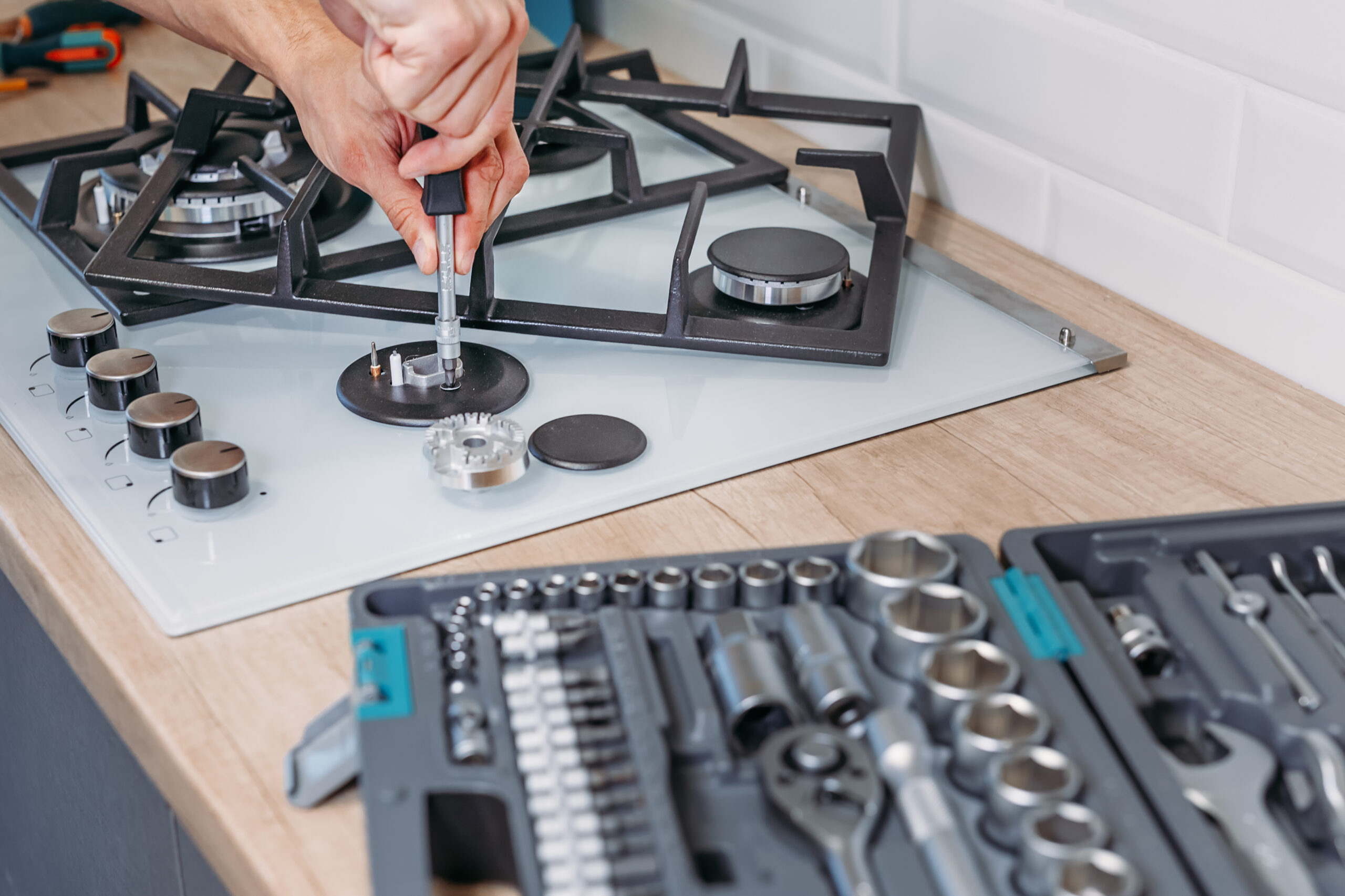 man hand repairs hotplate of gas panel with screwdriver